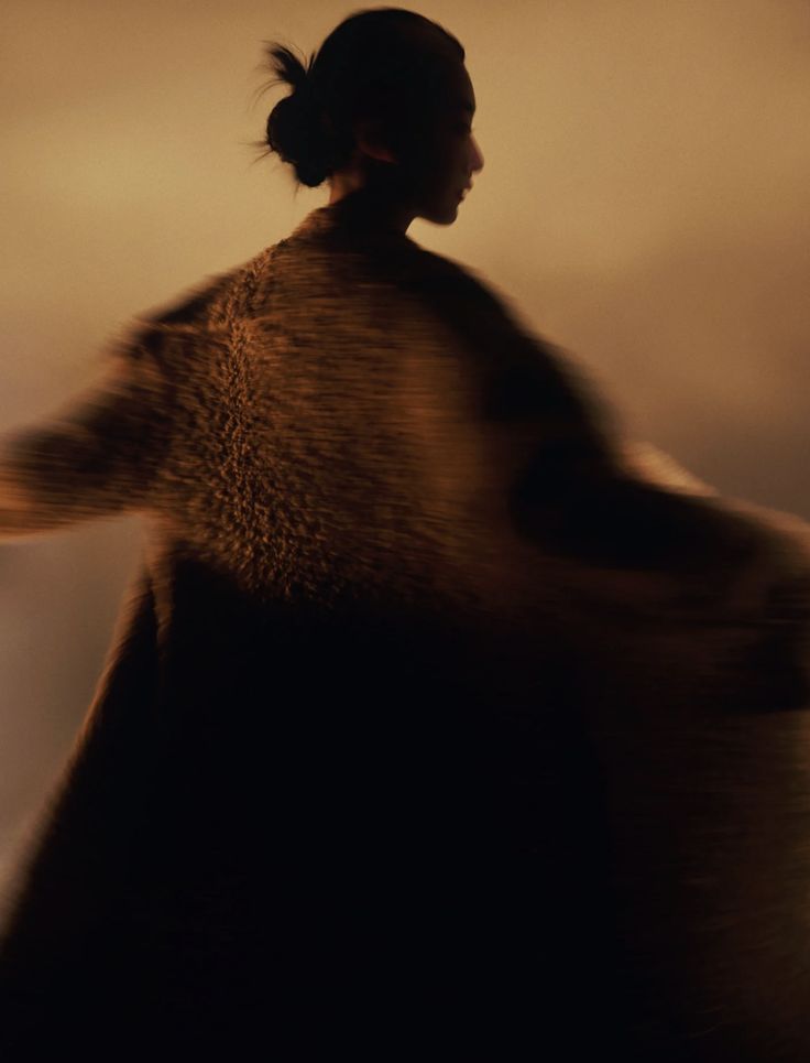 A woman turning in a textured coat, blurred in warm low light